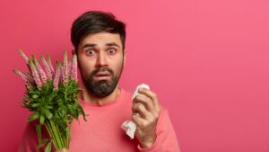 Photo of bearded man suffers from seasonal allergy, has itchy eyes and runny nose, holds napkin for