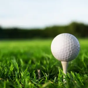 Close-up of a white golf ball on a tee in green grass on a sunny day on a golf course.