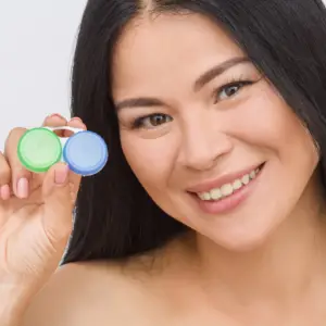 Smiling woman holding green and blue contact lens cases up to the camera.